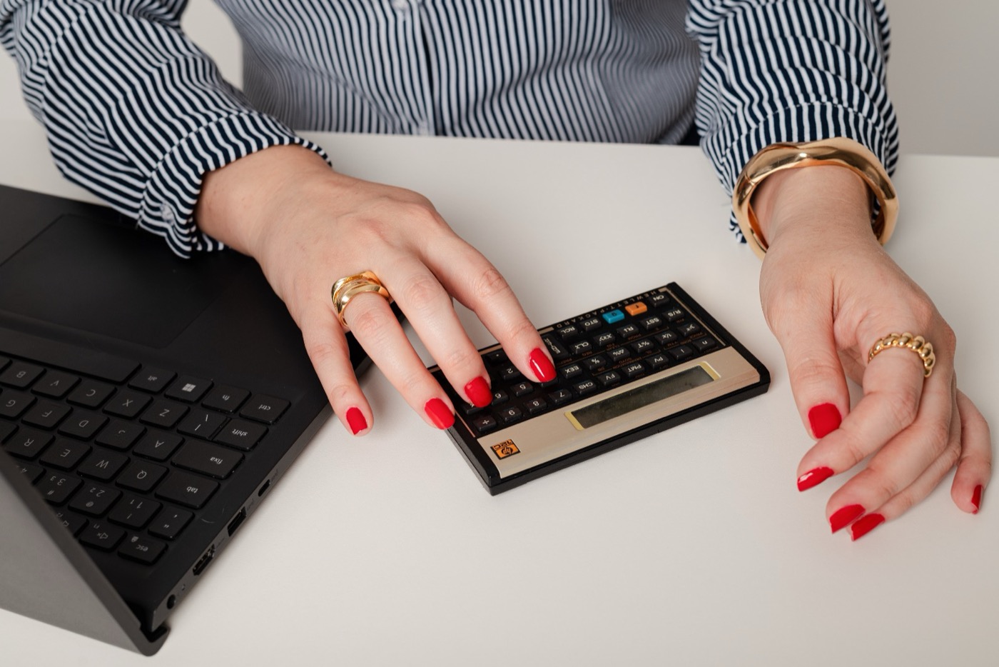 Mãos digitando em uma calculadora financeira ao lado de um notebook